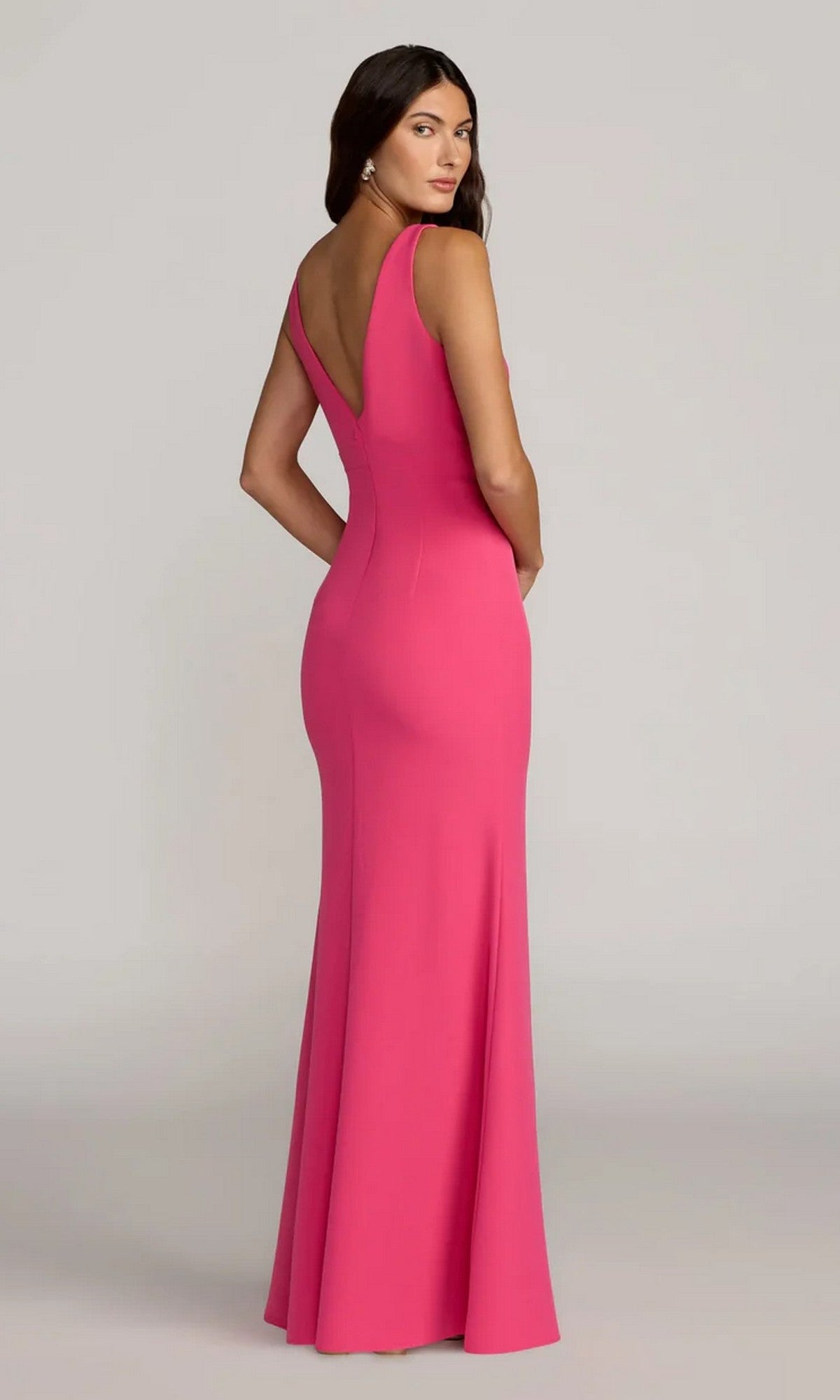 A woman models the Mac Duggal 2371, a sleeveless, fitted, floor-length pink crepe formal dress with a deep V-back, looking over her shoulder against a plain background.